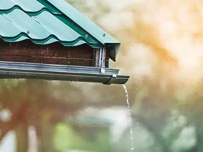 Canaleta semicircular de techo con tejas verdes, con agua cayendo durante precipitación