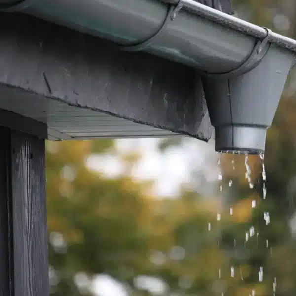 Canaleta gris con agua goteando durante la lluvia desde el alero del techo